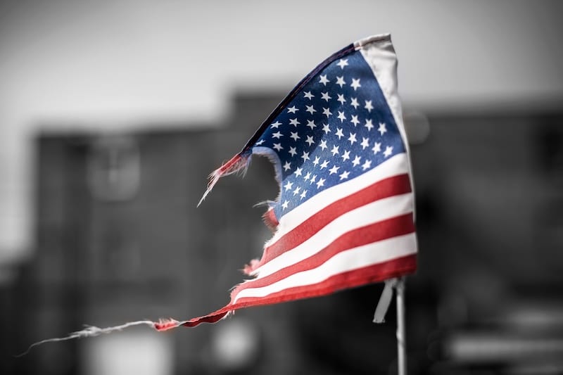 Trumpworld threat to democracy. black and white building blurred in the background and a ripped USA flag in the foreground